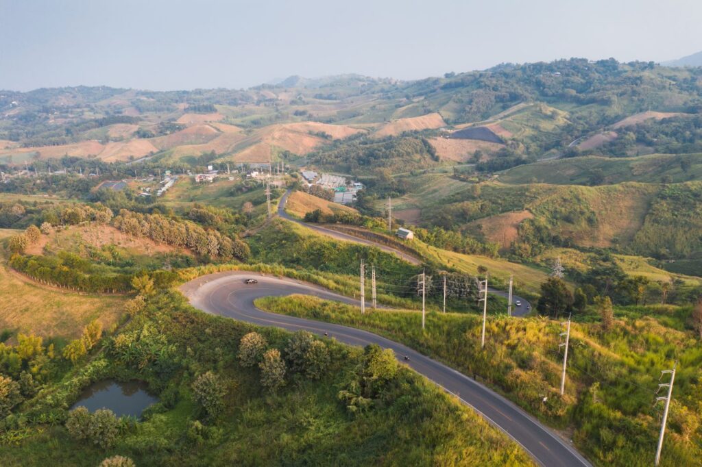 Scenery Of Curved Asphalt Road With Electric Pole On Green Hill